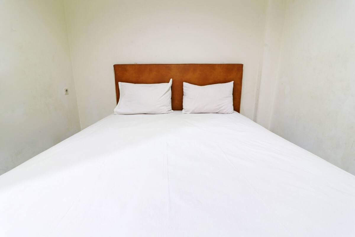 A single bed with a wooden headboard and two white pillows in a room with plain walls.