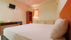 A hotel room with a bed, a desk, a television mounted on the wall, and a window with curtains. - Anno Guesthouse (Makassar)