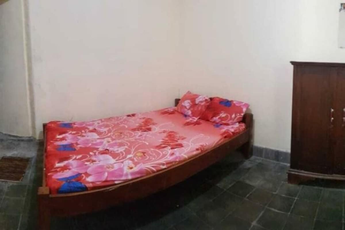 Una habitación pequeña con una cama individual, una colcha estampada con motivos florales y un armario de madera.