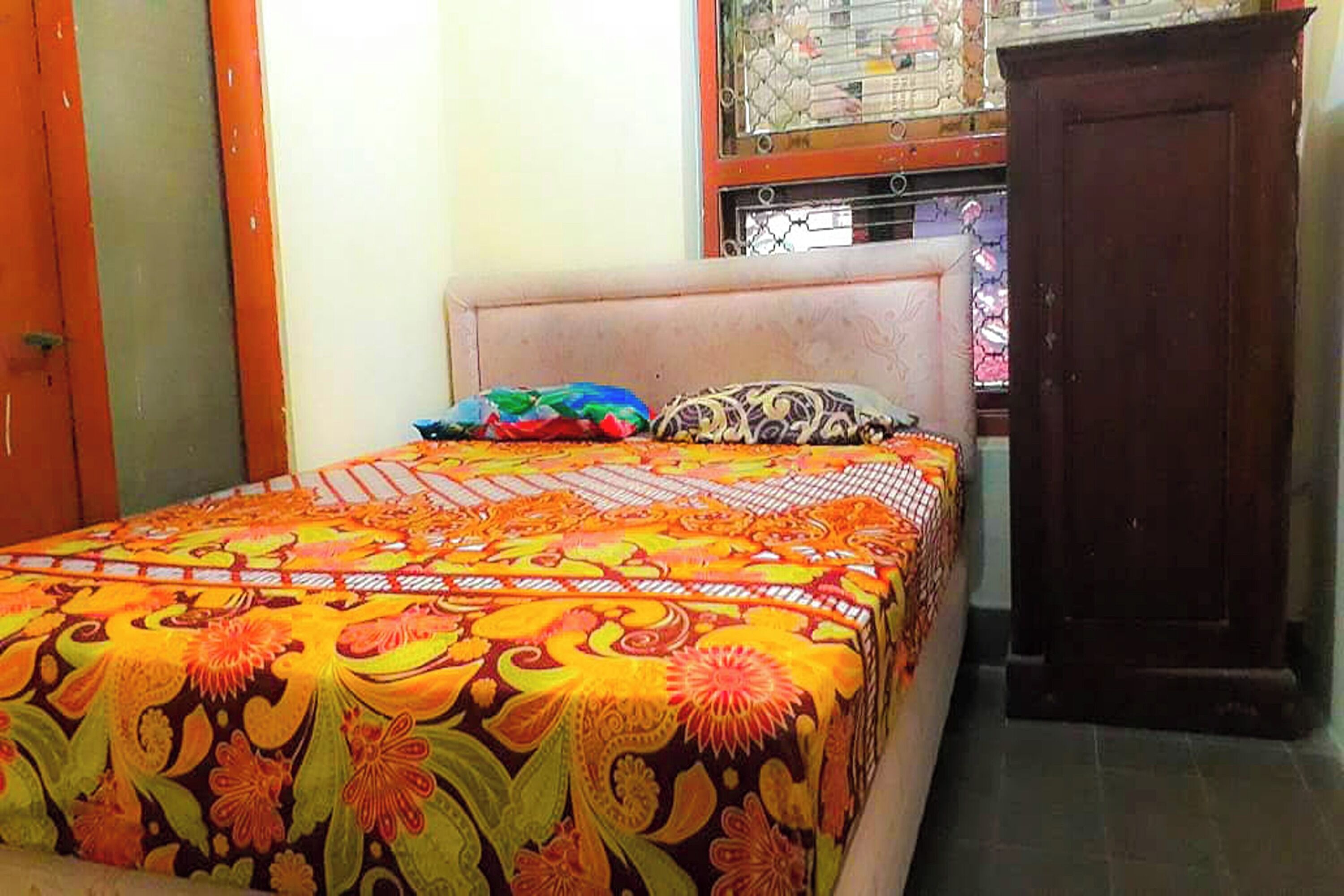 A bedroom with a bed, a window with a metal grill, and a wooden wardrobe.