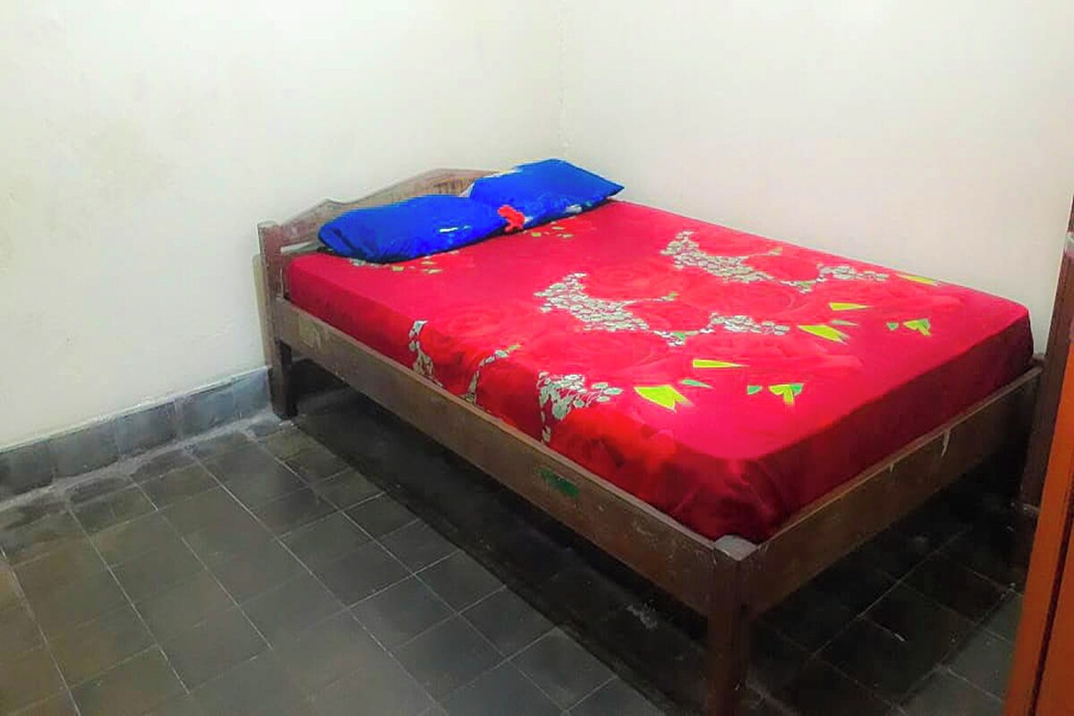 A small, single-bed room with a red bedspread and a blue pillow.