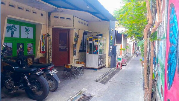 A narrow street with a motorcycle parked in front of a shop with a green door. - Losmen 2000 Tiga (Yogyakarta)