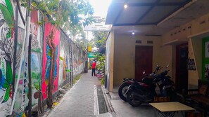A narrow alley with colorful murals on the walls, a motorcycle parked on the right, and a person in a red shirt walking away. - Losmen 2000 Tiga (Yogyakarta)