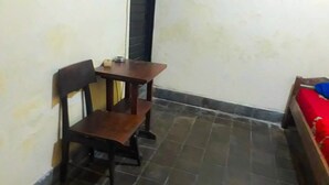 Una habitación pequeña con una silla de madera, una mesita y una cama roja.