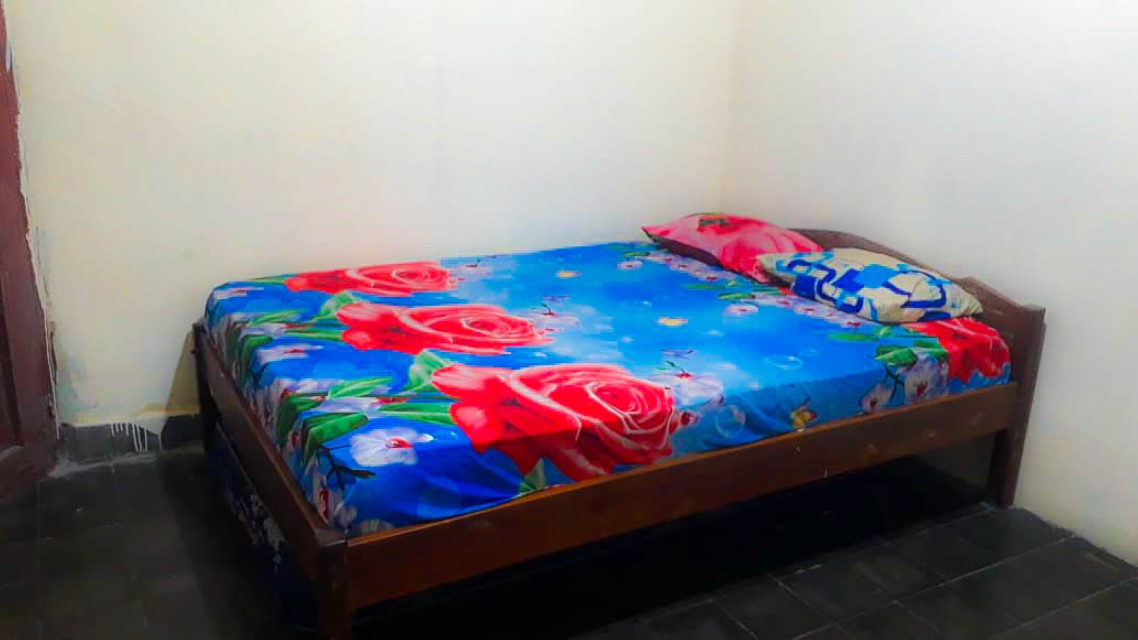 Una habitación pequeña con cama individual, cabecera de madera y colcha floral de colores.