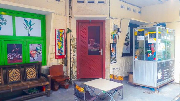 Una pequeña tienda rústica con una puerta verde, una roja y un refrigerador blanco.