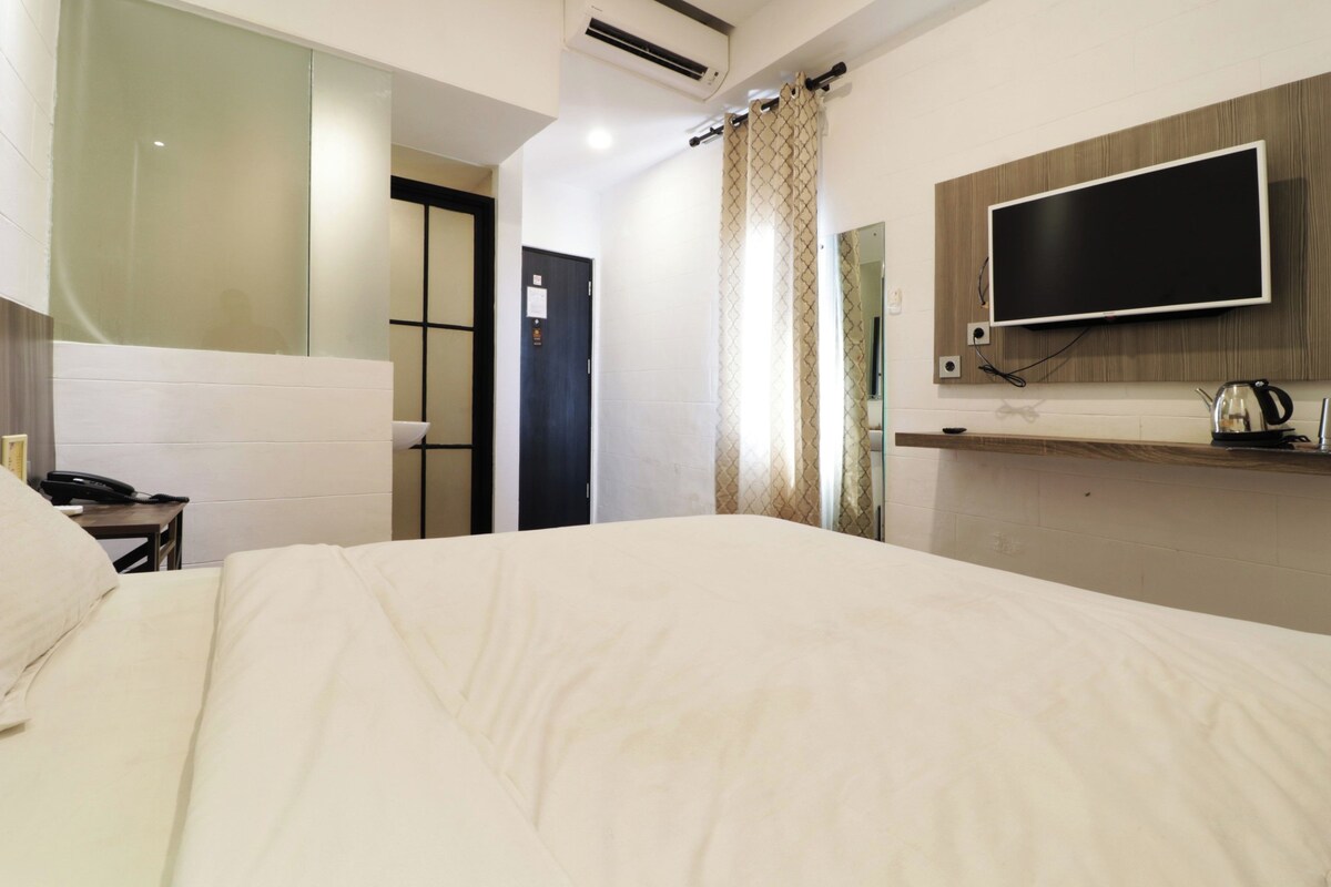 Habitación de hotel con una cama grande, un televisor de pantalla plana montado en la pared, una mesita de noche con un teléfono y una zona de ducha.