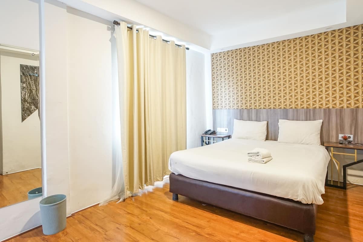 A hotel room with a large bed, a bedside table, a mirror, and a patterned wall.