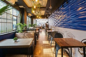 A modern restaurant interior with wooden tables and booths, potted plants, and a blue textured wall. - Hotel Sanrina Makassar (Makassar)