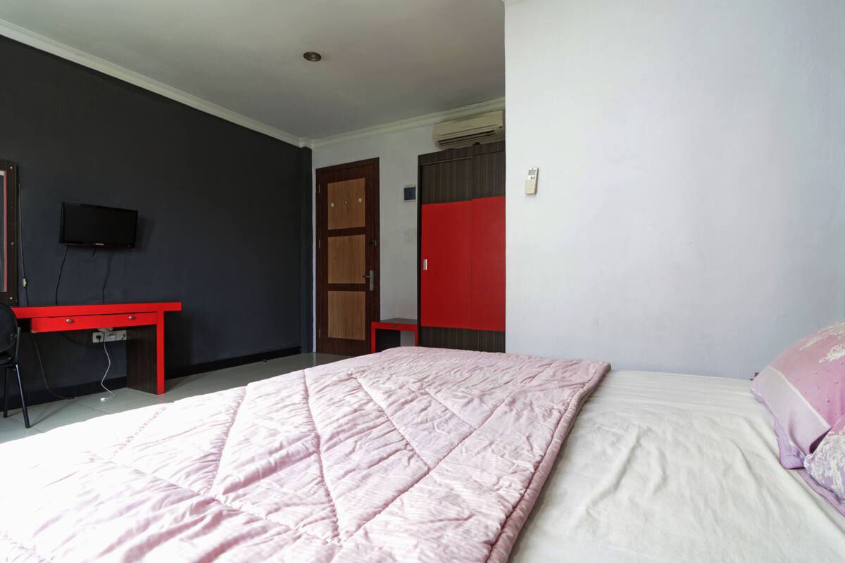 Een slaapkamer met een bed, een bureau, een televisie en een kledingkast.