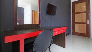 A room with a dark wall, a red desk with a mirror, a black chair, a flat-screen TV, and a wooden door. - Aurelia House A Mini Apartment (Pekanbaru)