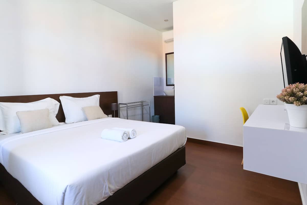 A hotel room with a large bed, a desk, a chair, and a mirror.