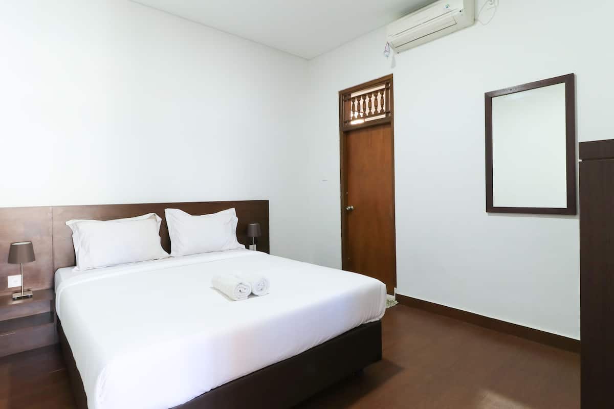 A hotel room with a large bed, a wooden headboard, a bedside table with a lamp, a wardrobe, and a mirror on the wall.