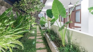 A narrow pathway with stepping stones, surrounded by lush greenery and large plants. - Kak Garden Inn (Kuta)