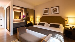 A hotel room with a large bed, a bedside table with a lamp, a nightstand with a phone, a chair, a mirror, and two framed pictures on the wall. - Casa Munfrà (Penango)