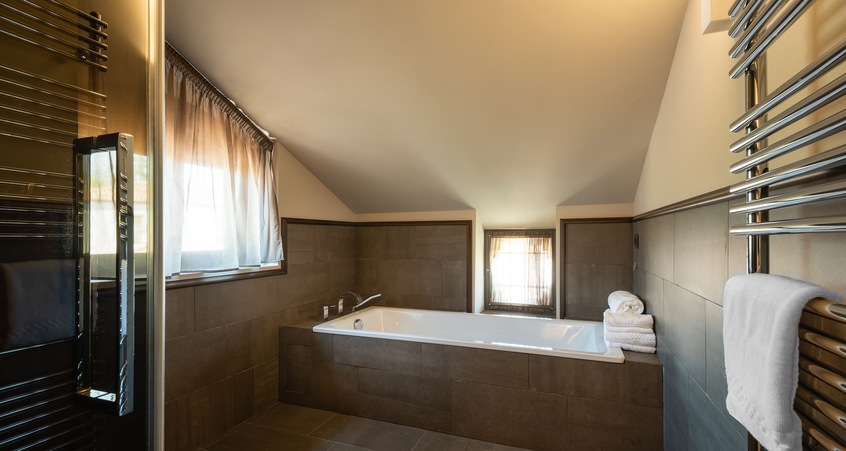 Un bagno moderno con una vasca da bagno ampia, una finestra con tende e un portasciugamani.