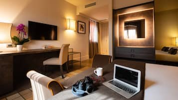 A hotel room with a desk, laptop, camera, and a potted orchid.