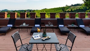 An outdoor seating area with lounge chairs and tables, a book, a glass of drink, and a plate of snacks. - Casa Munfrà (Penango)