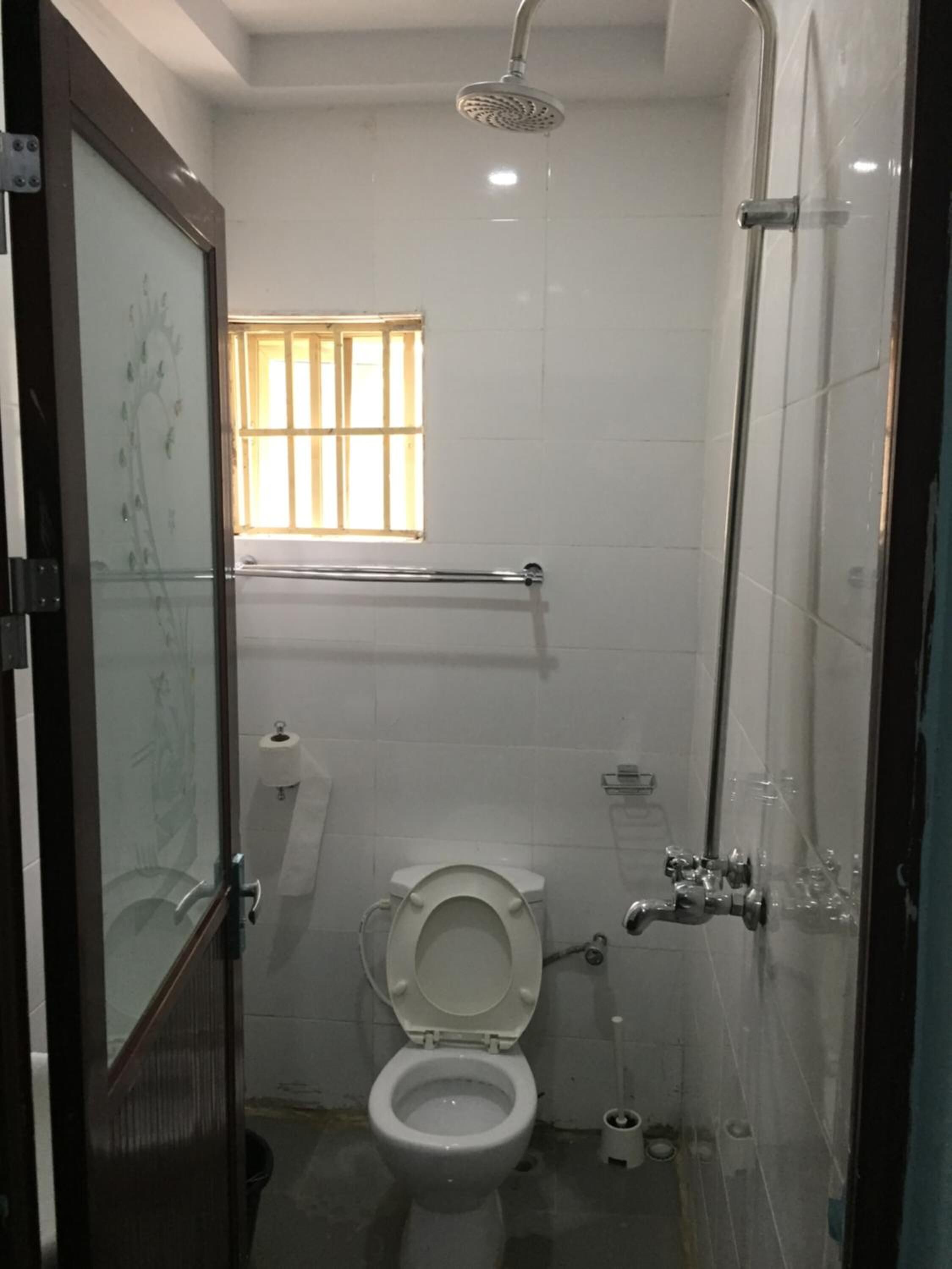 Een kleine, praktische badkamer met toilet, douche en raam.
