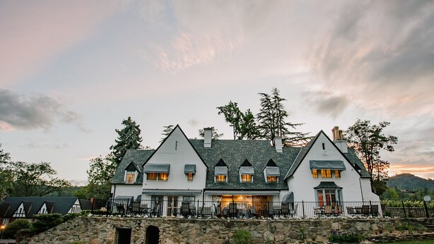 A large, white, multi-story house with a stone foundation, multiple chimneys, and a well-maintained lawn. - Hummingbird Estate Wine & Suites (Central Point)