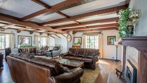 A spacious living room with leather sofas, a fireplace, and wooden beams on the ceiling. - Hummingbird Estate Wine & Suites (Central Point)
