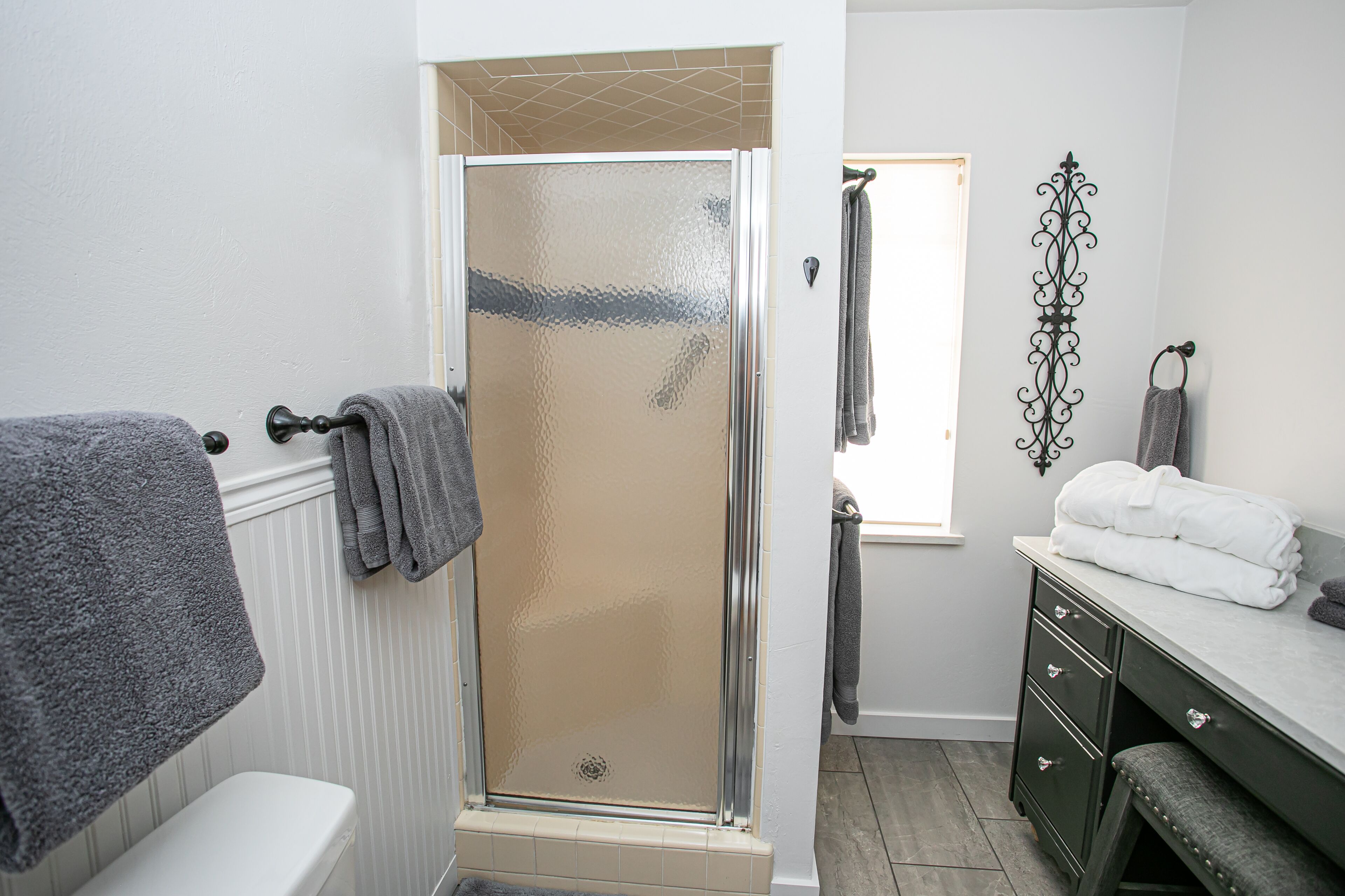 A bathroom with a shower, a toilet, a vanity with a mirror, and towels on the wall.