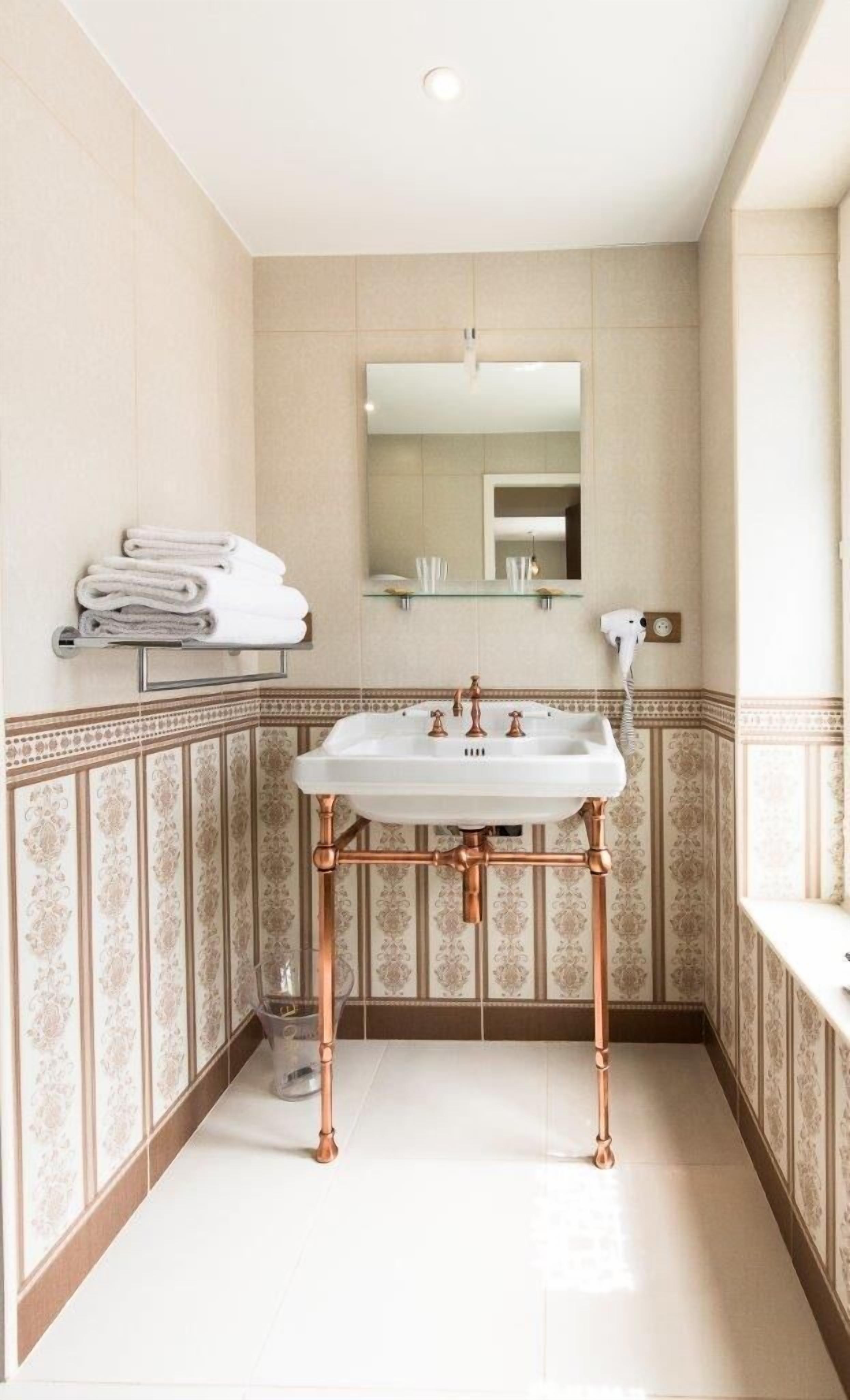 A bathroom with a white sink, copper pipes, and patterned wallpaper.