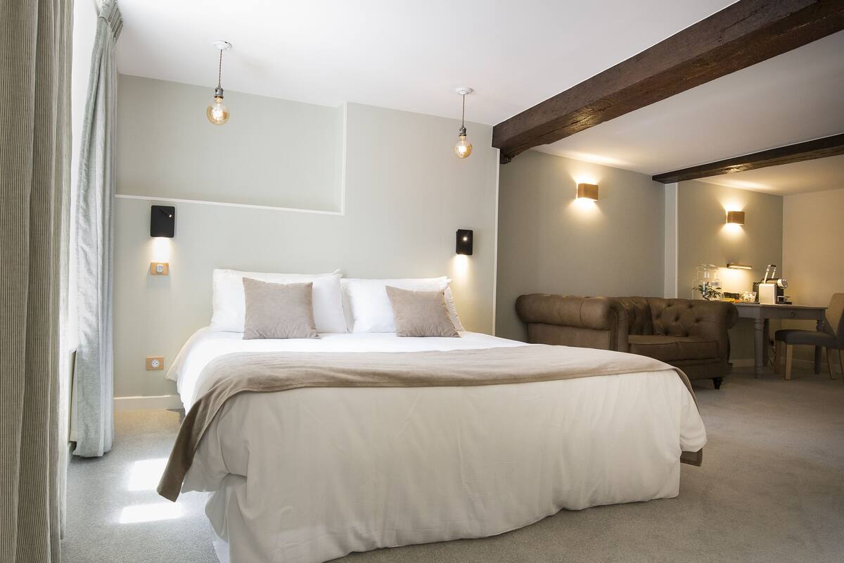 A bedroom with a large bed, a desk, and a chair. There are wall-mounted lights and a ceiling light.