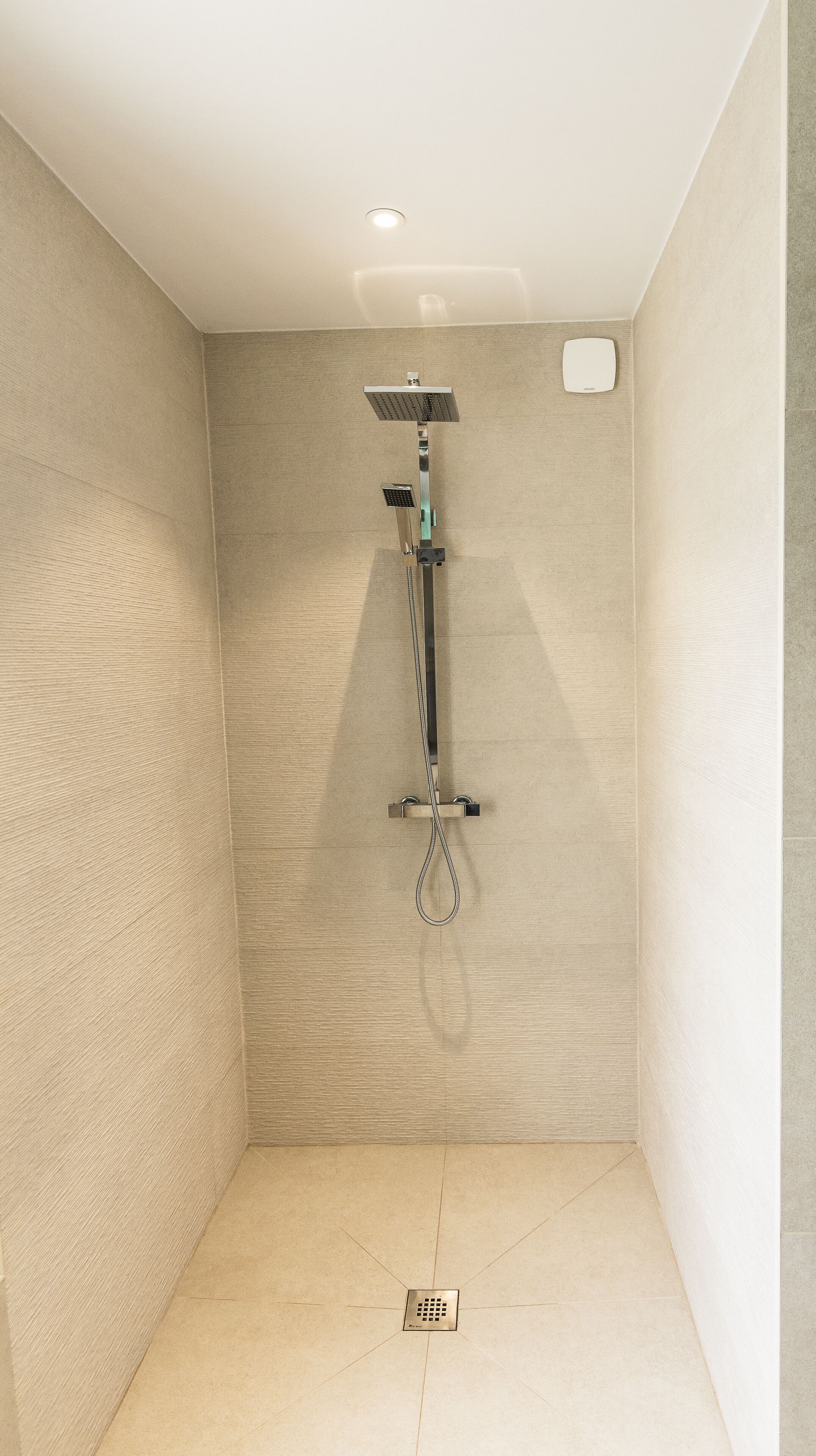 A modern shower with a square showerhead and a handheld shower attachment.