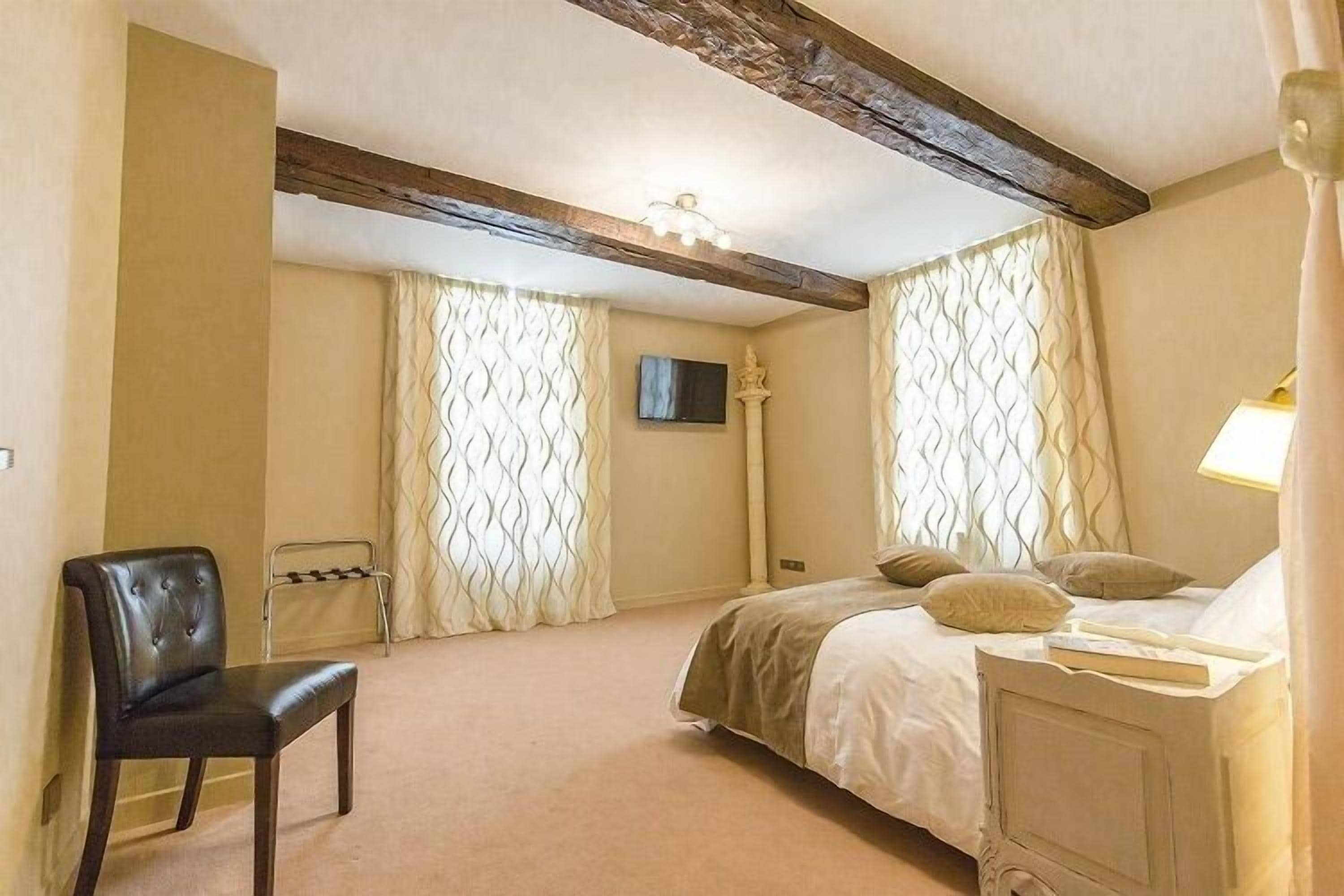 A bedroom with a bed, a chair, a desk, and a television on the wall.
