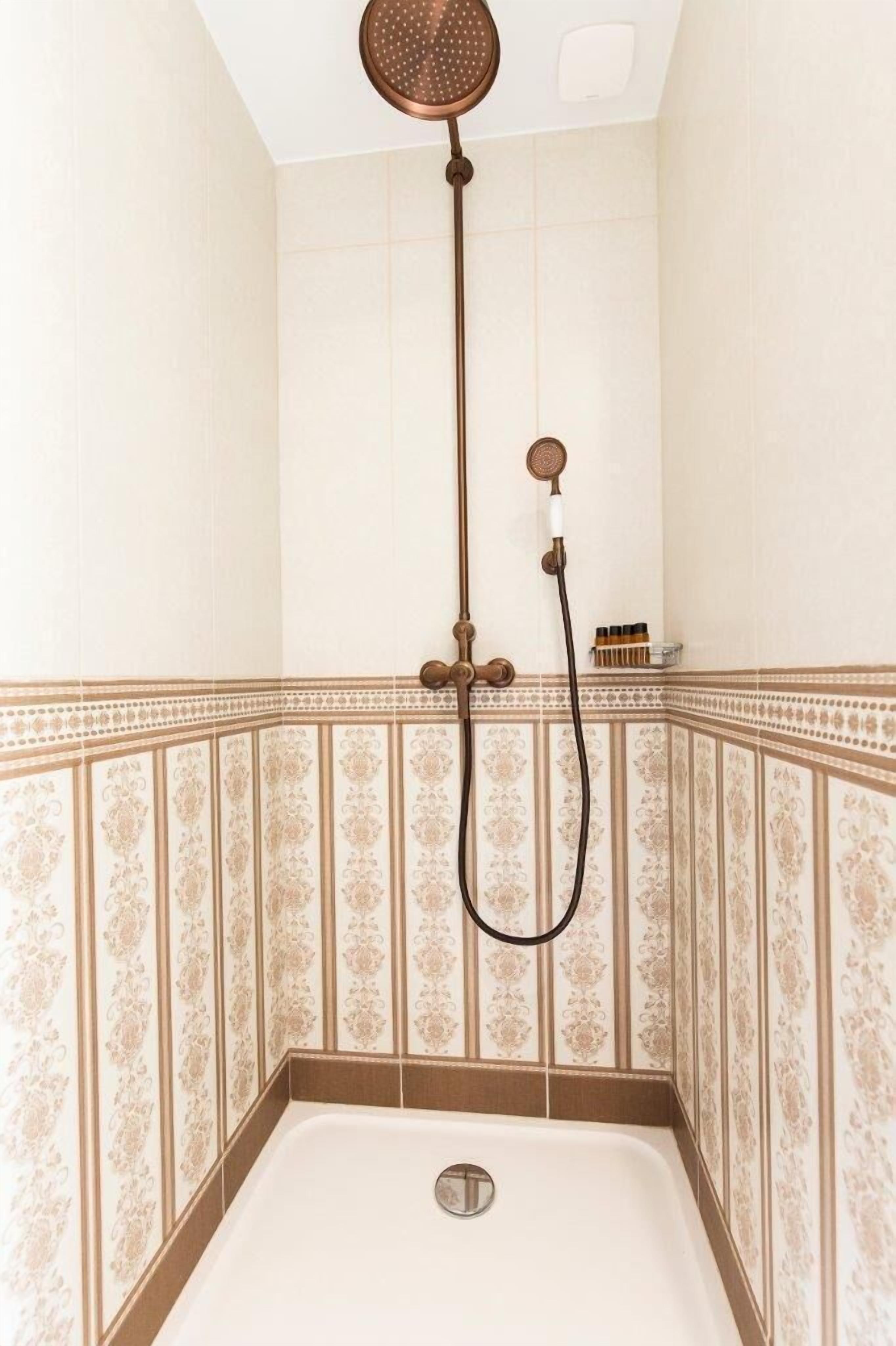 Een douche met een handdouche en een muurbevestigde kraan in een badkamer met betegelde muren.