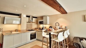 Une cuisine moderne avec des armoires blanches, une poutre en bois au plafond, un four à micro-ondes encastré et un coin repas avec des chaises blanches.