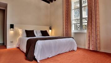 A bedroom with a bed, a window with patterned curtains, and a view of a building with arches.