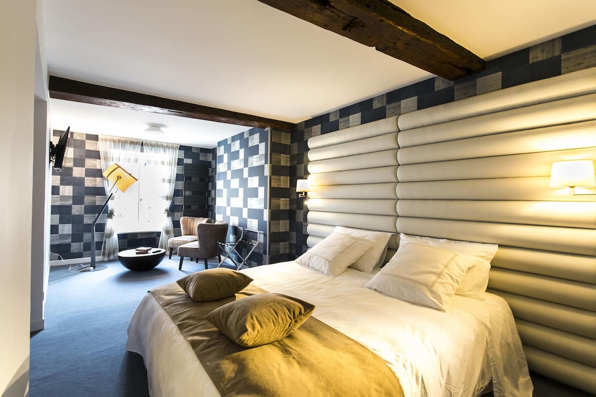 A modern hotel room with a large bed, a seating area with a round table, and a checkered wall pattern.