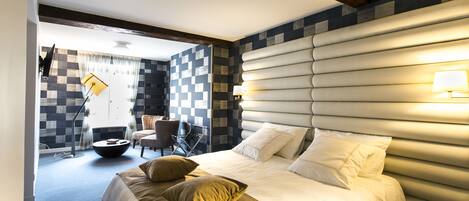 Una habitación de hotel moderna con una cama grande, un área de descanso con una mesa redonda y un patrón de pared a cuadros.