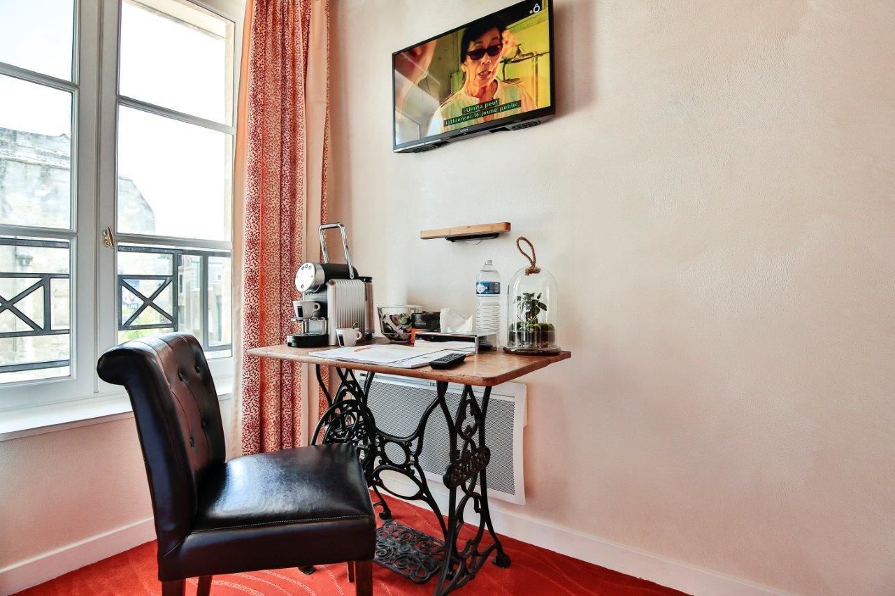Ein Zimmer mit einem schwarzen Ledersessel, einem kleinen Tisch mit Heizkörper und einem an der Wand befestigten Fernseher sowie einem Fenster mit Blick auf Gebäude.