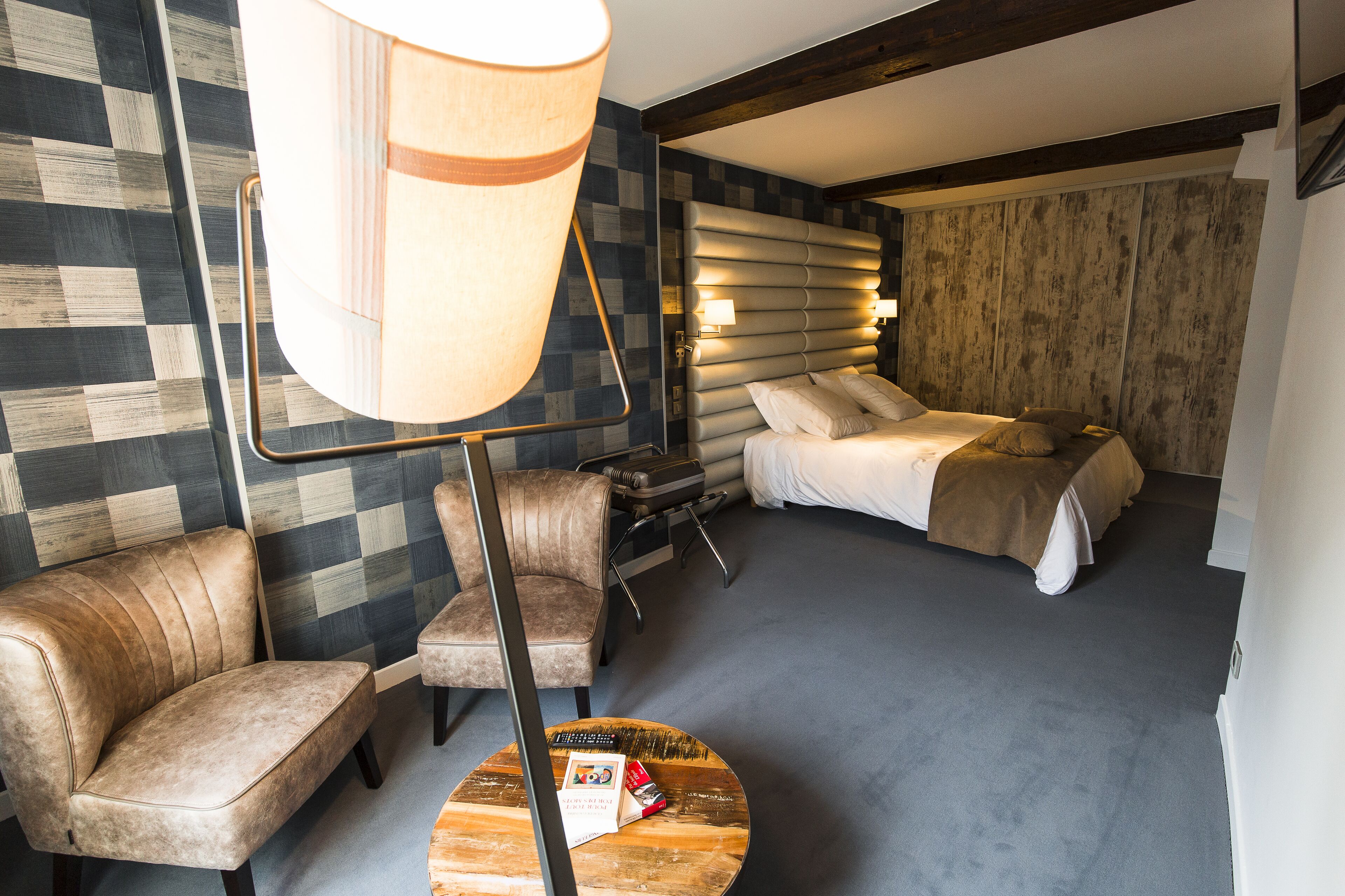 Quarto de hotel com parede xadrez, uma cama com cabeceira, um sofá, uma mesa de centro e um abajur.