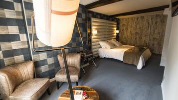 Quarto de hotel com parede xadrez, uma cama com cabeceira, um sofá, uma mesa de centro e um abajur.