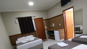 Ein Hotelzimmer mit drei Einzelbetten, einem an der Wand befestigten Fernseher und einer Tür zu einem weiteren Zimmer.