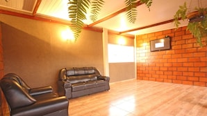 Ein Zimmer mit zwei schwarzen Ledersofas, Holzboden, Backsteinwand und einem an der Wand befestigten Fernseher.