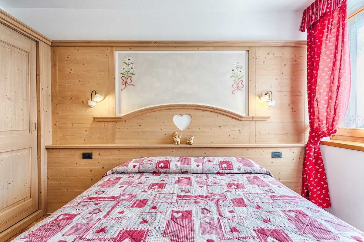 A bedroom with a wooden headboard, a quilted bedspread, and a window with red curtains.