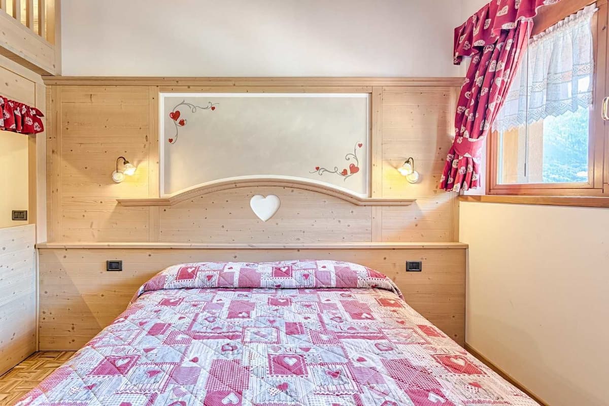 A bedroom with a wooden headboard, a large mirror, a heart-shaped decoration, and a patterned bedspread.
