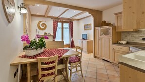 A cozy kitchen with wooden cabinets, a dining table with chairs, and a TV. - Residence Ronchi (Molveno)