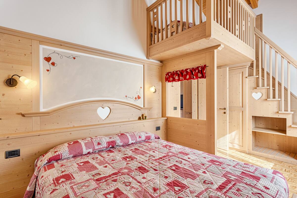 A wooden bedroom with a bunk bed, a bed with a patterned quilt, and a headboard with heart decorations.