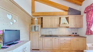 A compact kitchen with wooden cabinets, a microwave, and a tiled backsplash. - Residence Ronchi (Molveno)