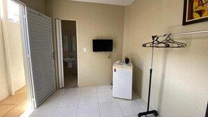 A room with a sliding door, a small refrigerator, a TV mounted on the wall, and a clothes drying rack.