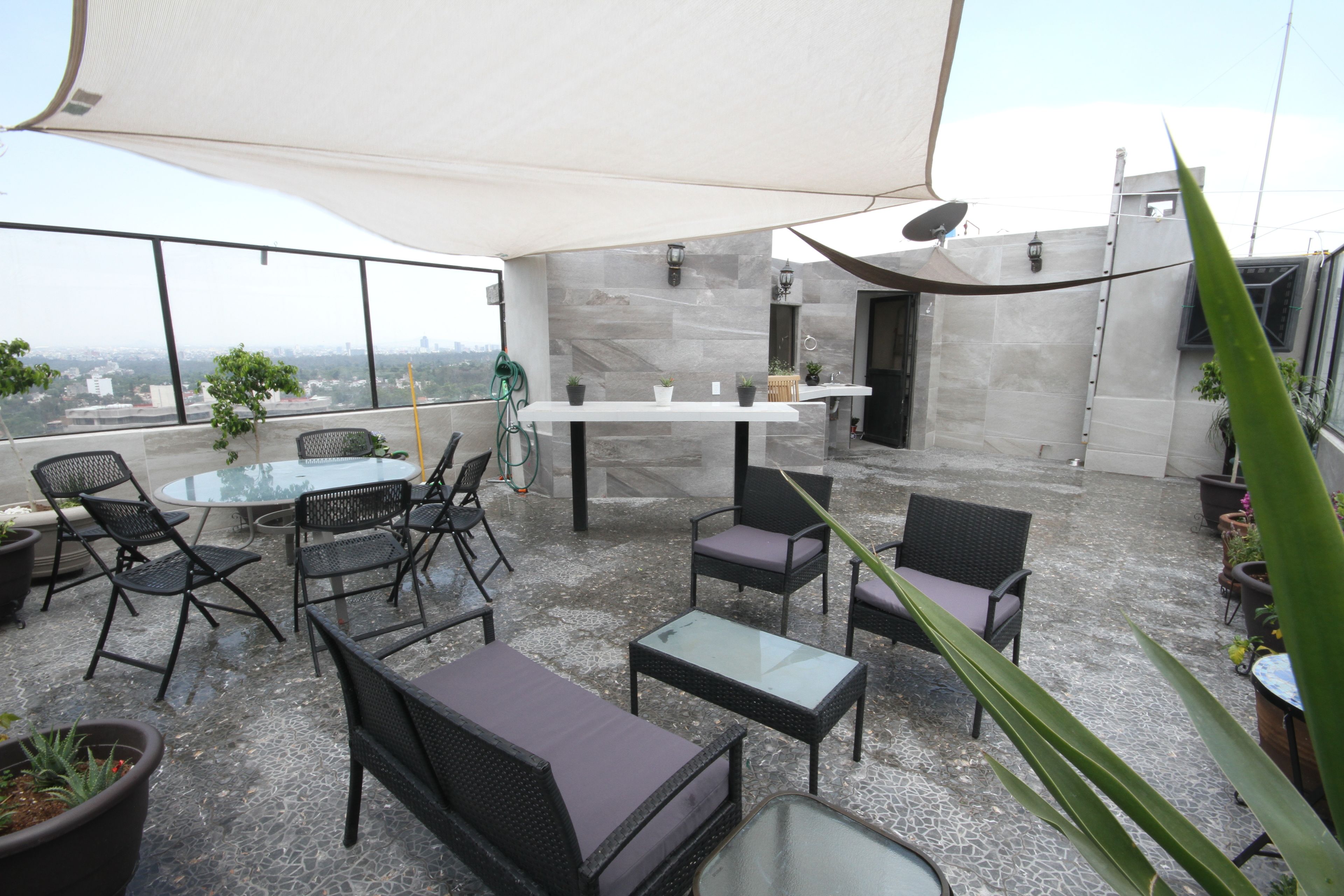 A rooftop patio with outdoor furniture, a glass table, and potted plants.