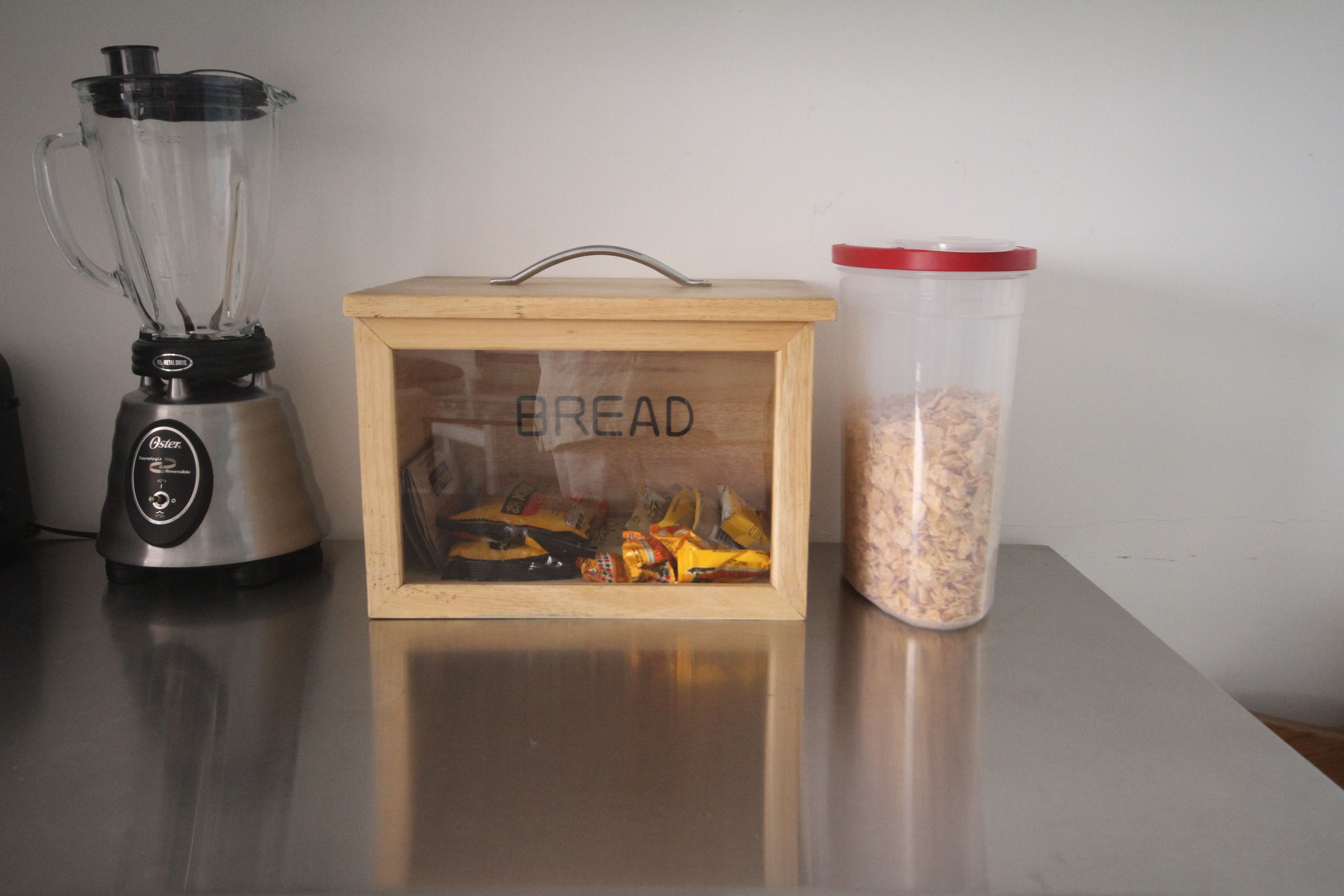 Un plan de travail de cuisine avec un mixeur, une boîte à pain en bois et un récipient rempli de flocons d’avoine.