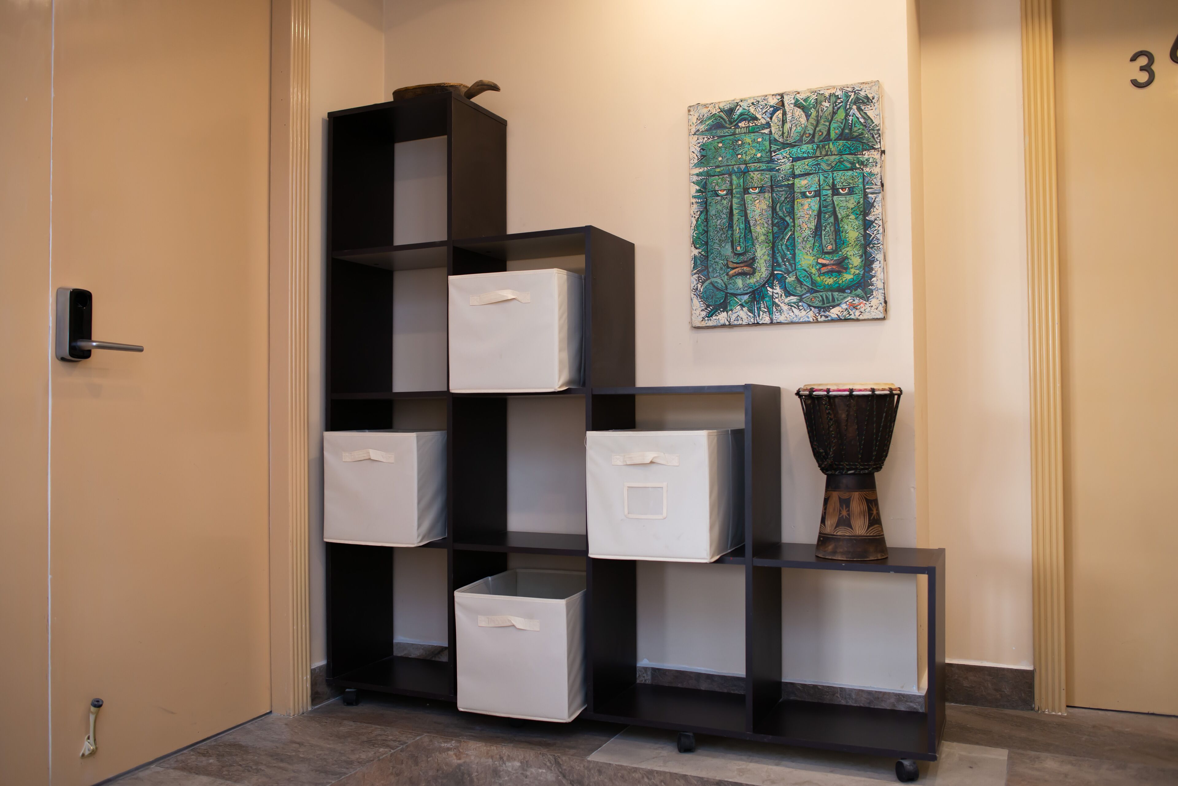 A hallway with a black shelving unit containing white storage boxes, a decorative vase, and a wall art piece.