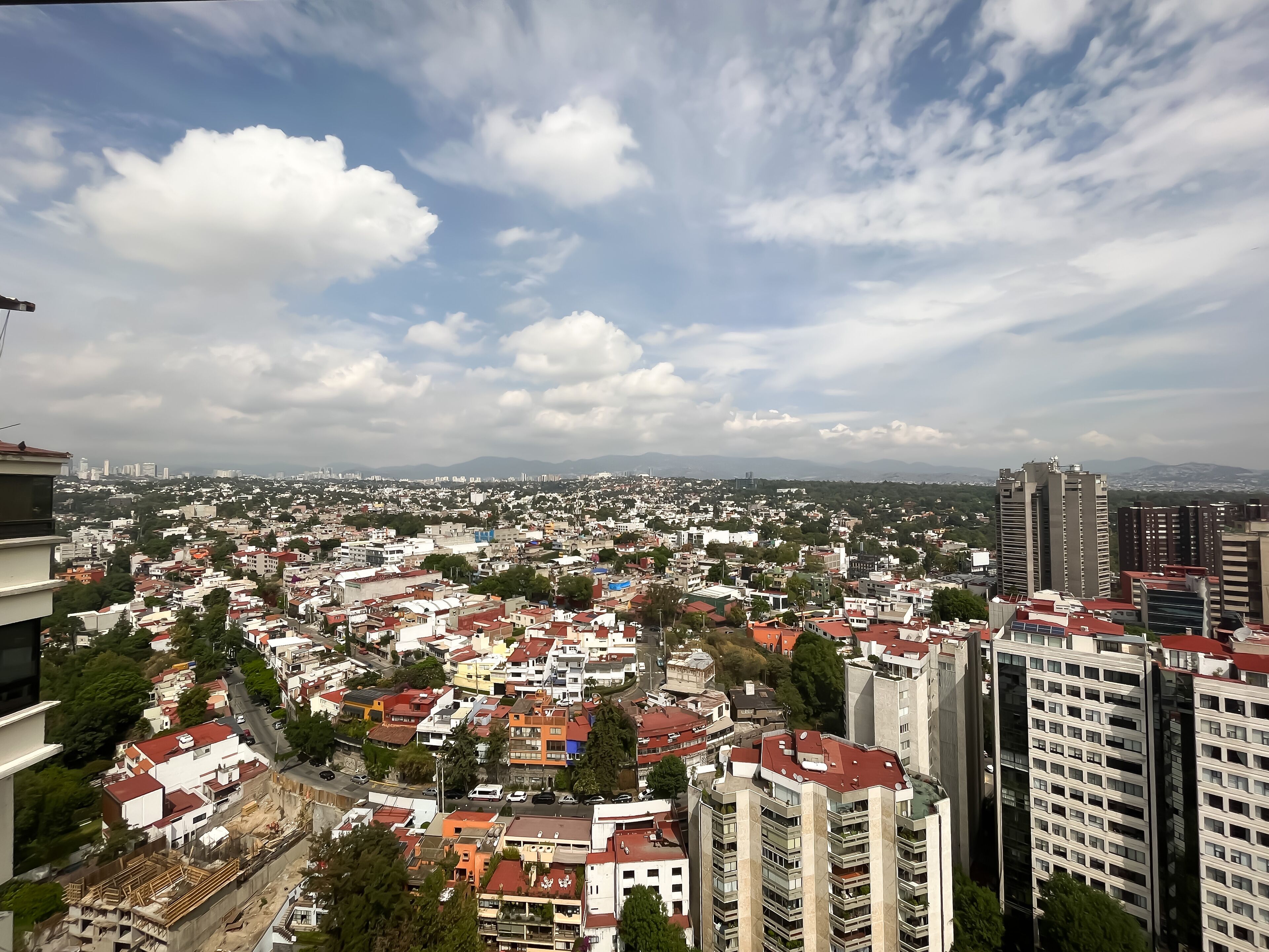 A cityscape with a mix of residential and high-rise buildings, a clear sky, and distant mountains.